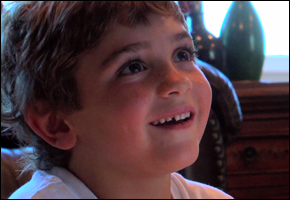 A young boy smiles as he looks upward at a television.