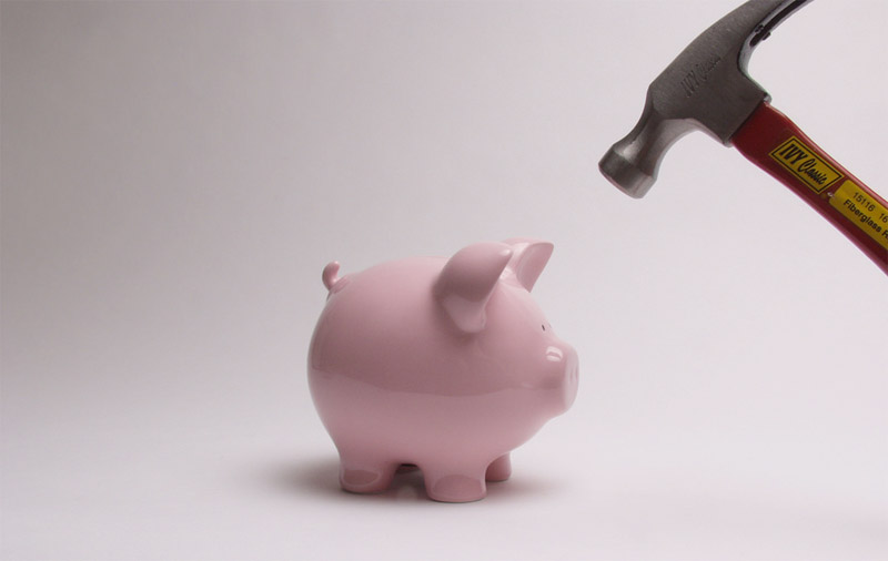A hammer is poised above a piggy bank.