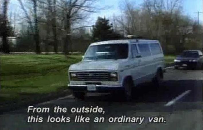 Video capture of a white van driving on a road. Captions are white italic letters that read From the outside, this looks like an ordinary van.