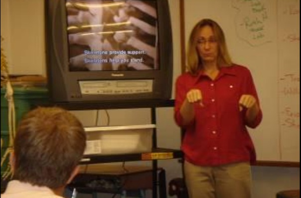 Scharla Becker signs in front of a captioned video in her class.