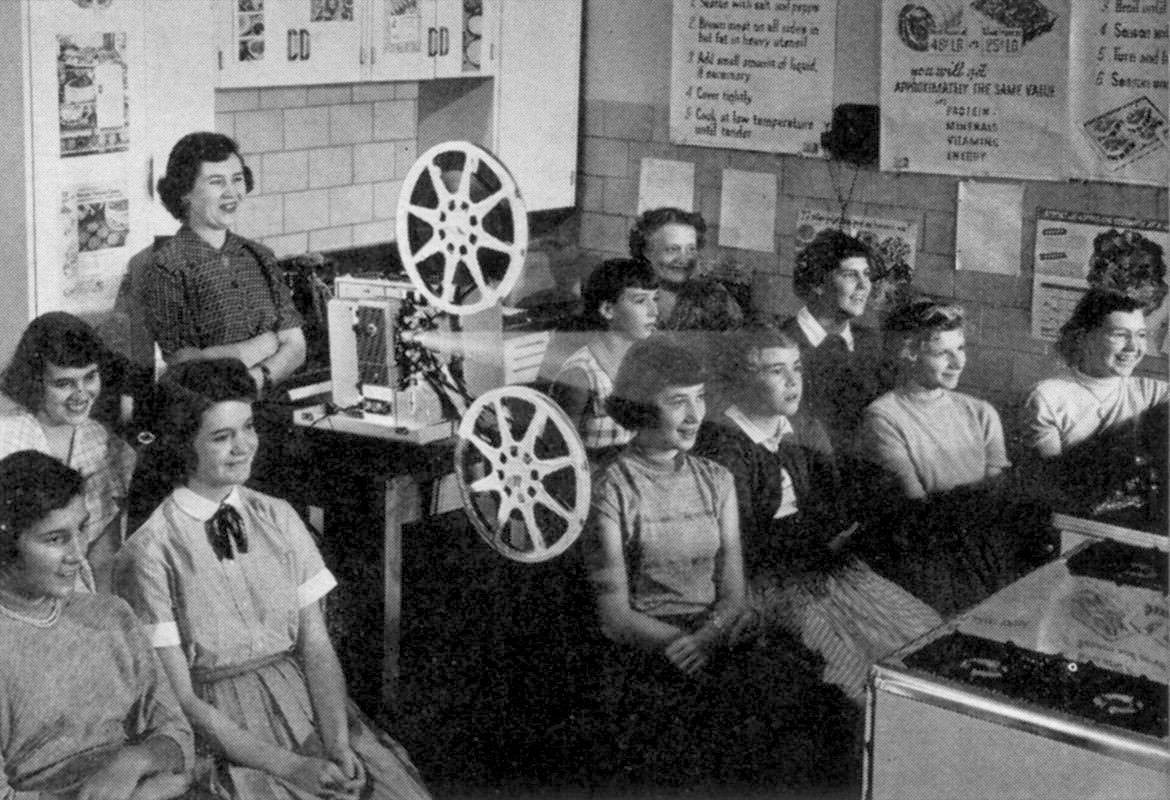 Black and white photo of a reel to reel film being shown in a classroom.