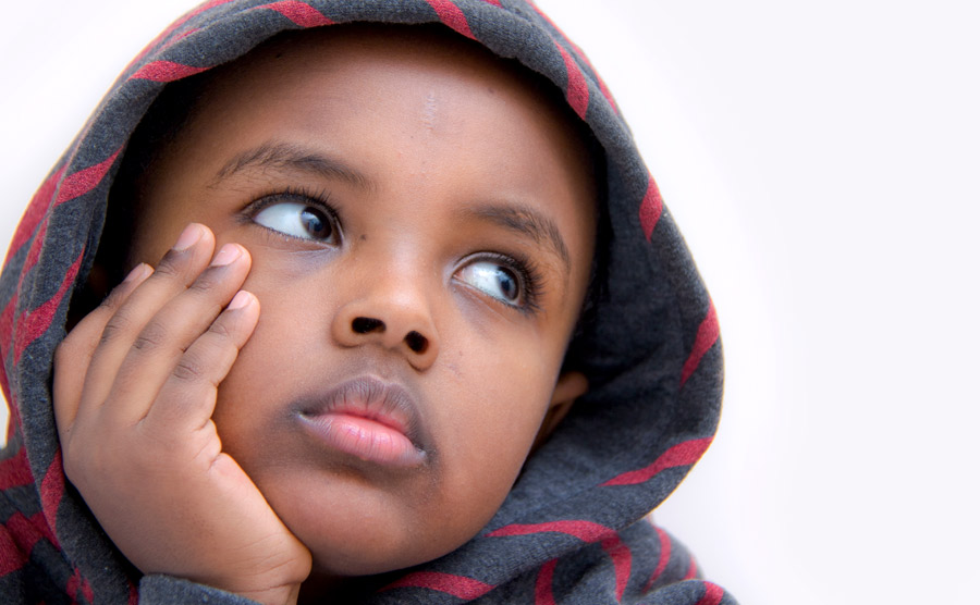 A young child rests his face on his hand and looks thoughtful.