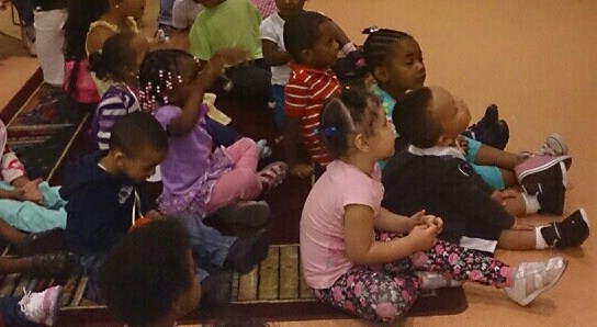 Children sit on the floor in a classroom.