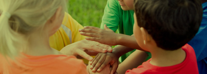 Children stand in a circle and place their hands together.