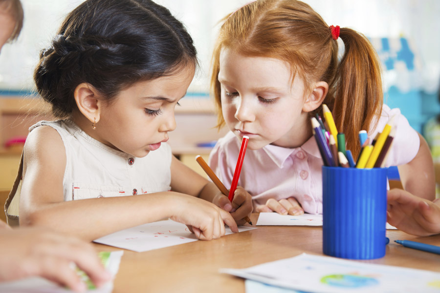 Two young girls work at a table together at school.