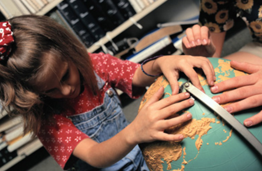 A young blind girl has her hands on a large globe.