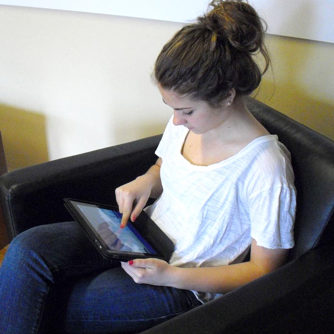 A teen girl sits in a comfy chair and uses her computer tablet.