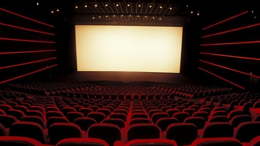 Movie theater with rows of seats and a large rectangular screen as wide as the theater in front.