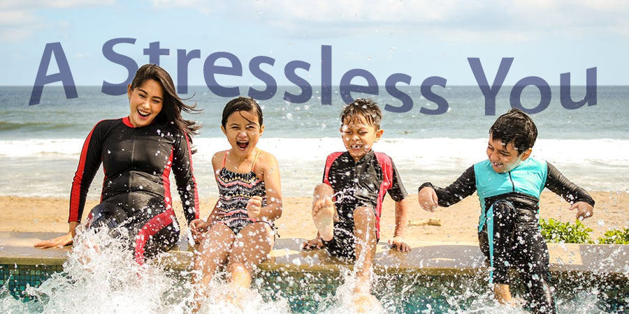 A woman and three children at the beach sit and splash the water with their feet. Words: A stressless you.