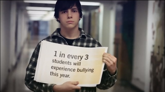 A boy holds a sign that says One in every three students will experience bullying this year.
