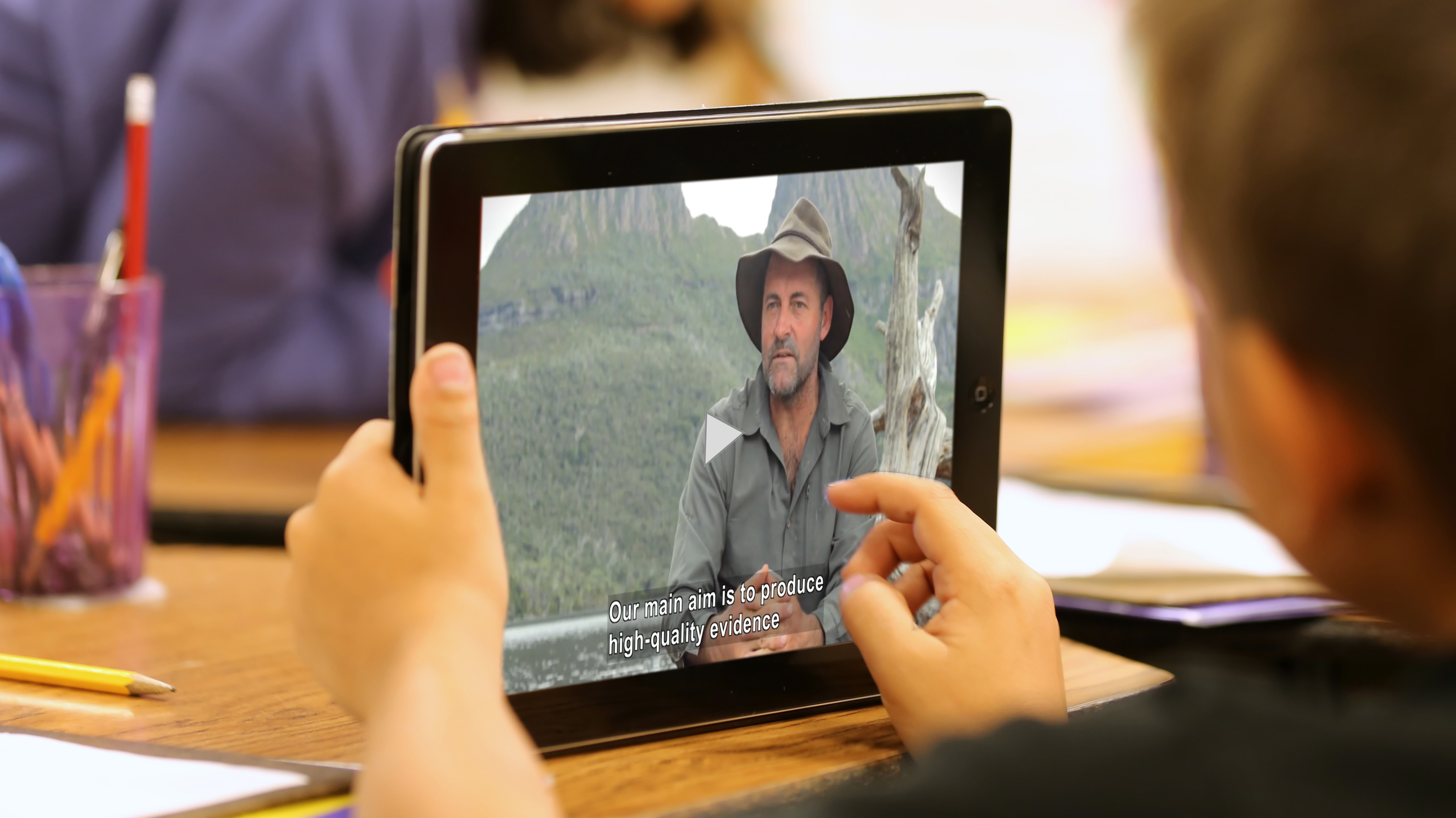 A student holds a computer tablet that is playing a captioned video.