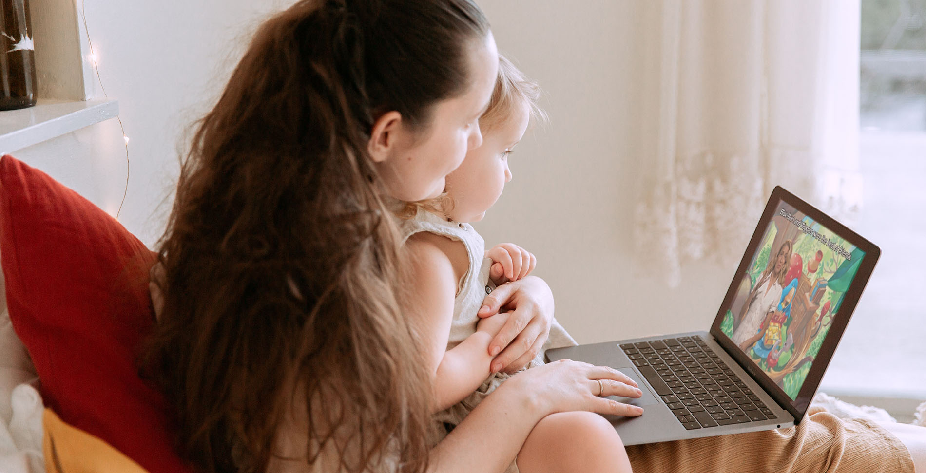 A monther and baby sit at home watching a video on a laptop.