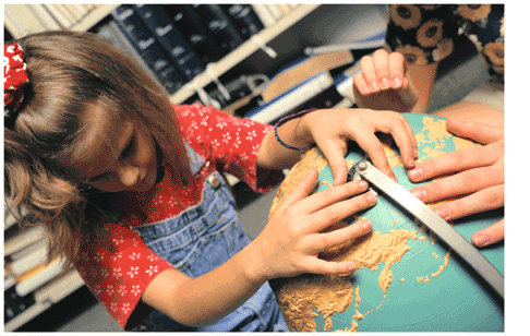 A blind third-grade girl feels a topographical globe in a classroom.