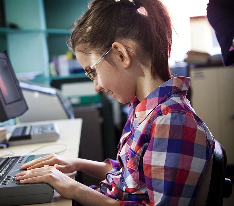 A young girl wearing glasses uses a refreshable braille device.