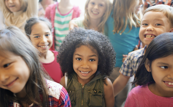 Several young children of different ethnic backgrounds smile.