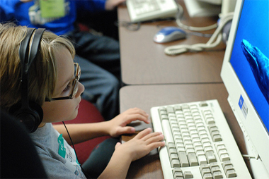a elementary school student wears headphones and watches a computer monitor, where a whale is partially visible.