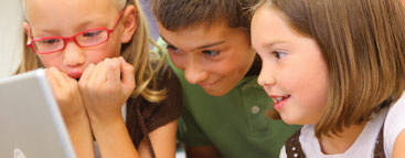 Two young girls and a boy smile as they watch a video monitor