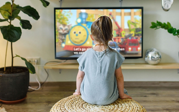 A young girl sits on a cushion in front of a television.
