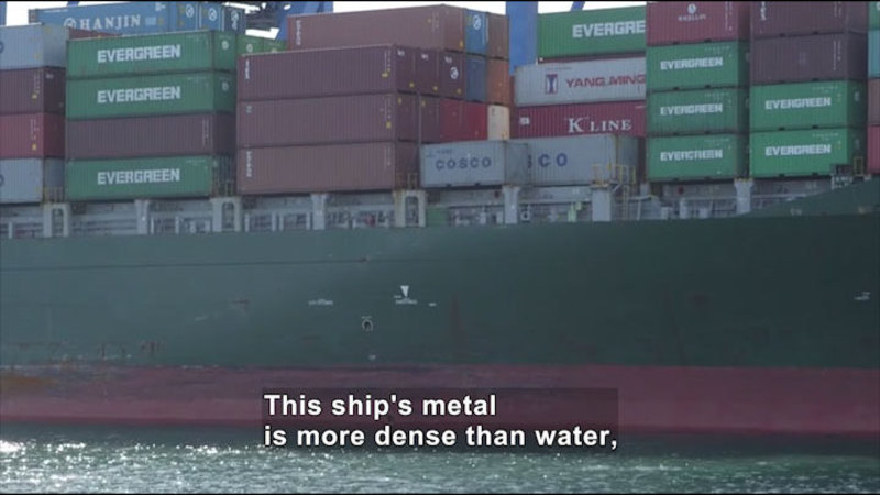 Metal shipping containers on the deck of a cargo ship. Caption: The ship's metal is more dense than water,