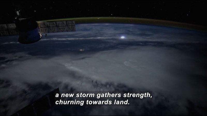 Satellite looking down the surface of the Earth over a large storm system. Caption: a new storm gathers strength, churning towards land.