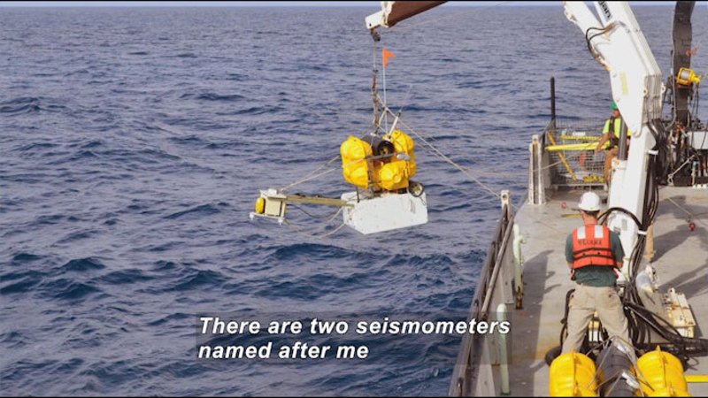 Ship with industrial equipment and a crane lowering something into the water. Caption: There are two seismometers named after me