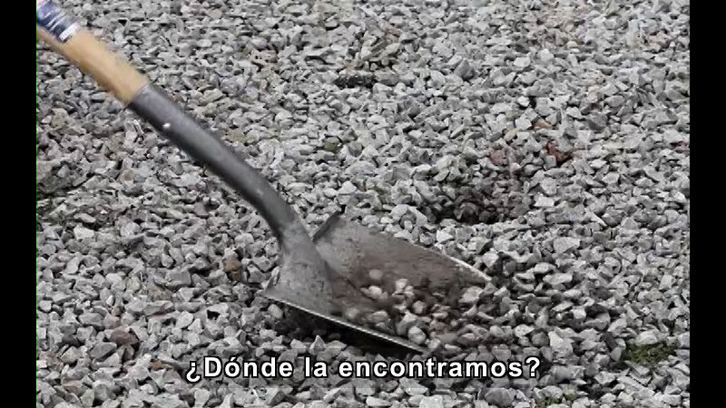 Shovel digging into gravel. Spanish captions.