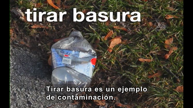 Crushed plastic soda bottle on the ground. Spanish captions.