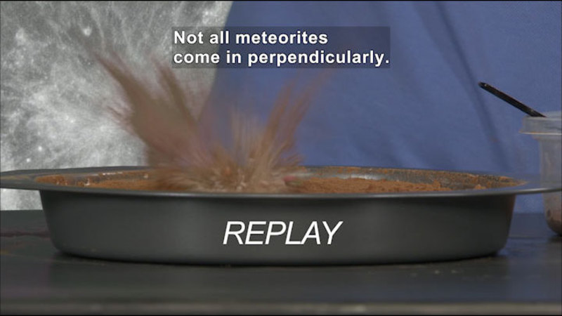 Object striking dirt and throwing up debris. REPLAY. Caption: Not all meteorites come in perpendicularly.