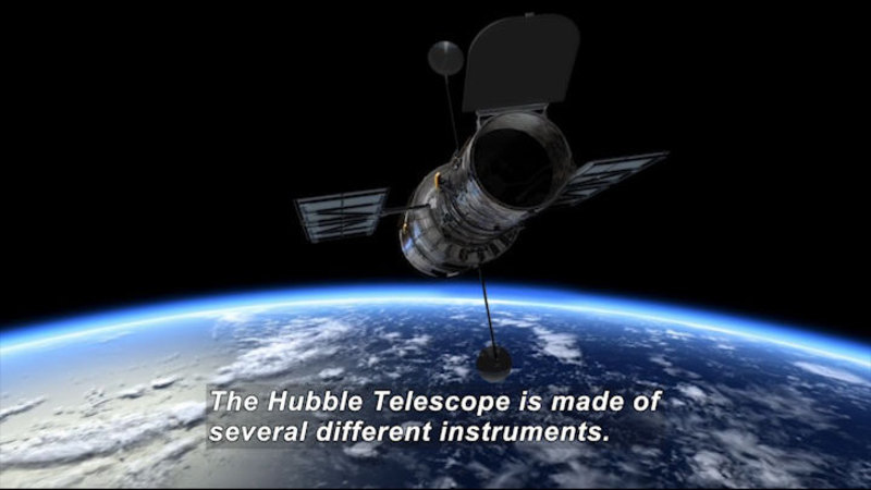 A cylindrical space craft with two solar wings and two rods capped in spheres protruding from it in relief over the planet Earth and space. Caption: The Hubble Telescope is made of several different instruments.