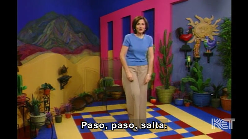 Person standing in a colorful room with cacti in pots all around the walls. Spanish captions.