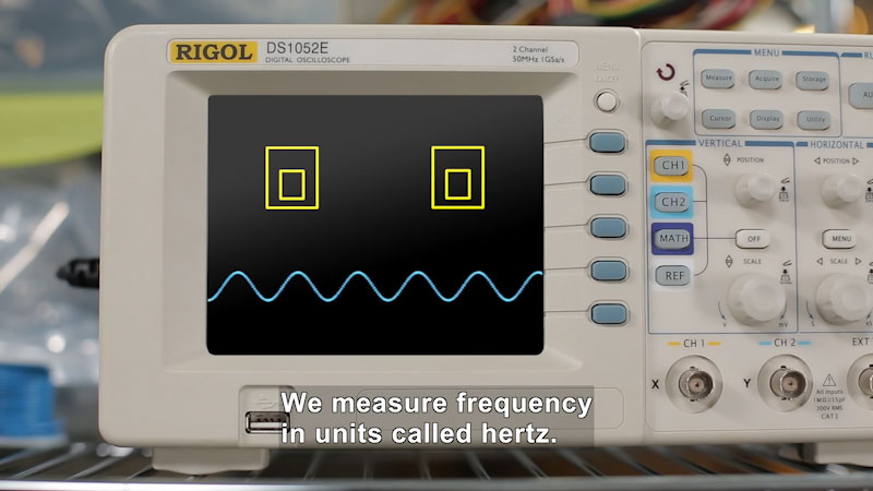 Machine labelled DS1052E Digital Oscilloscope with a wavy line across the screen and complex controls. Caption: We measure frequency in units called hertz.