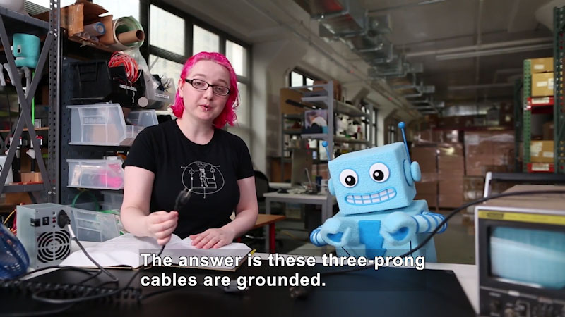 Person in a workshop holding a power cord with three prongs. Caption: The answer is these three-prong cables are grounded.