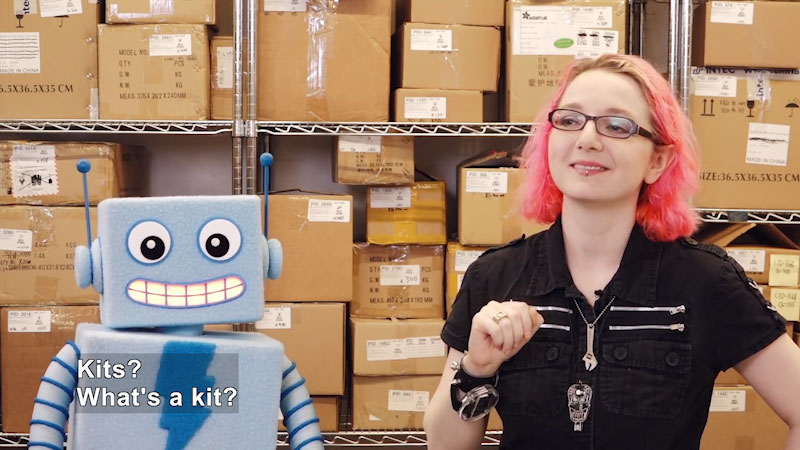 Person and a robot standing in front of shelves full of boxes. Caption: Kits? What's a kit?