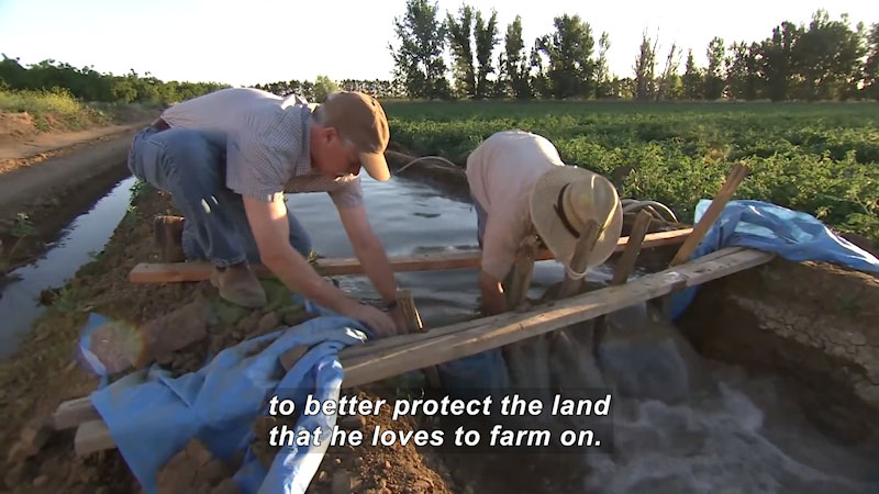 Two people working on an irrigation channel. Caption: to better protect the land that he loves to farm on.