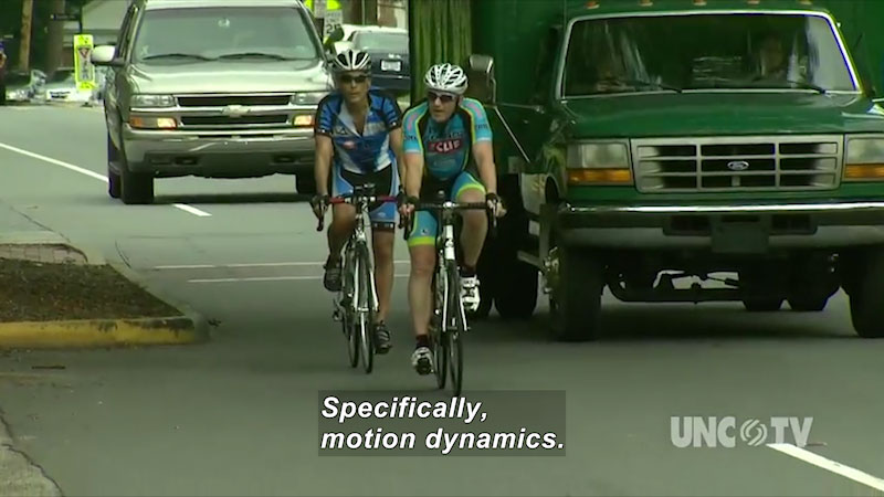 Two bicyclists on a city street with vehicles. Caption: Specifically, motion dynamics.