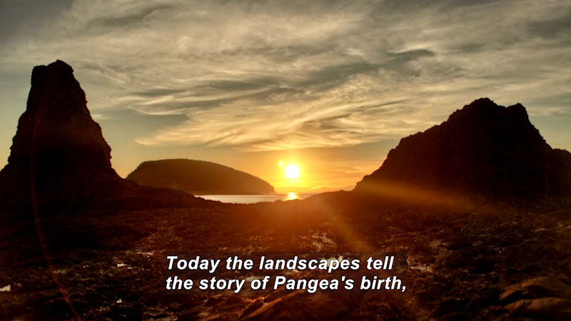 Sun setting between two rocky outcroppings over a body of water. Caption: Today the landscapes tell the story of Pangea's birth,