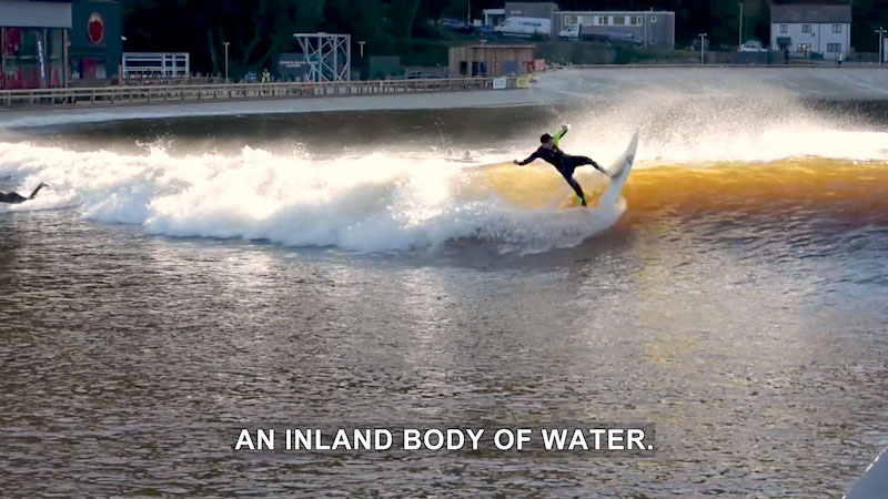 Person surfing with the beach behind them. Caption: An inland body of water.