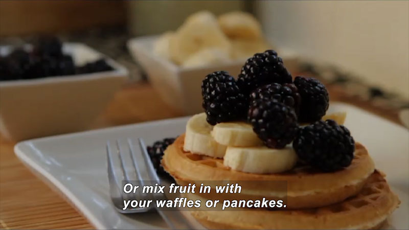 Waffles topped with sliced bananas and blackberries. Caption: Or mix fruit in with your waffles or pancakes.