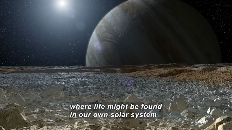 Rocky, flat, barren landscape with a large planet covered in bands of color on the horizon and a star in the distance. Caption: where life might be found in our own solar system