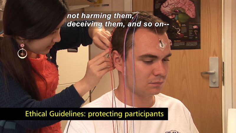 Person attaching wires with adhesive to the head of a second person. Ethical guidelines: protecting participants. Caption: not harming them, deceiving them, and so on --