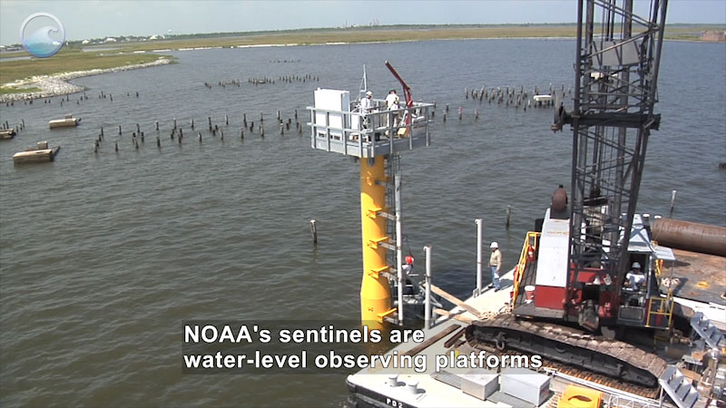 Platform with large machinery and people on it floating in the water close to shore. Caption: NOAA's sentinels are water-level observing platforms