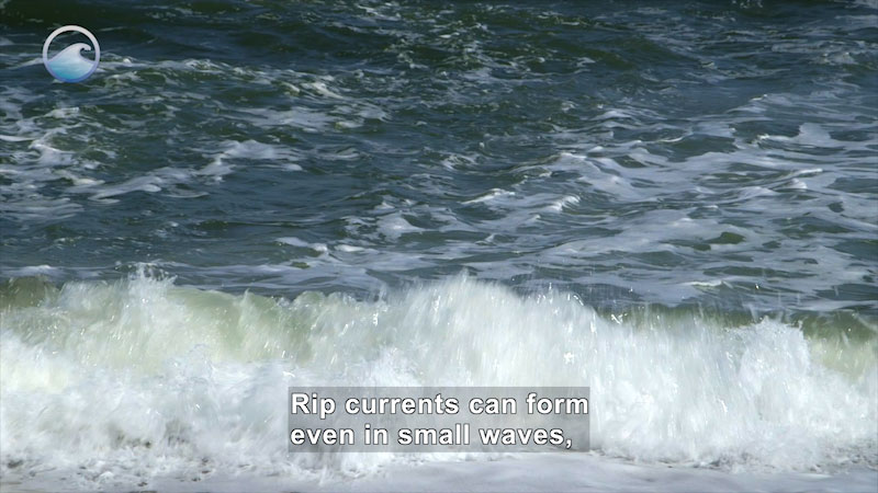Close up of a wave crashing on shore. Caption: Rip currents can form even in small waves,