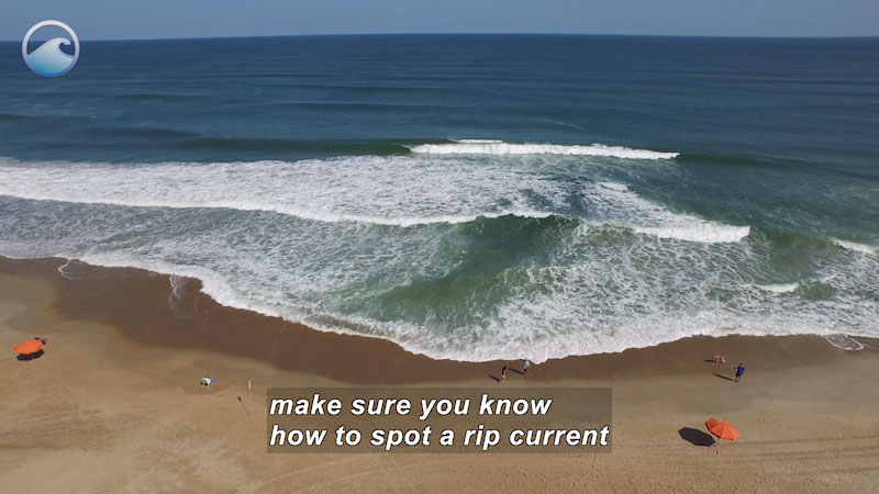 Aerial view of apparently calm waves meeting the shore while a few people walk on the beach. Caption: make sure you know how to spot a rip current