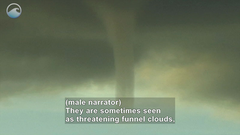 Grayish-green cloudy sky with a funnel cloud reaching to the ground. Caption: (male narrator) They are sometimes seen as threatening funnel clouds,