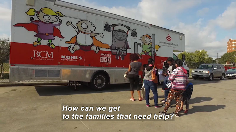 People lined up outside a mobile health clinic. Caption: How can we get to the families that need help?