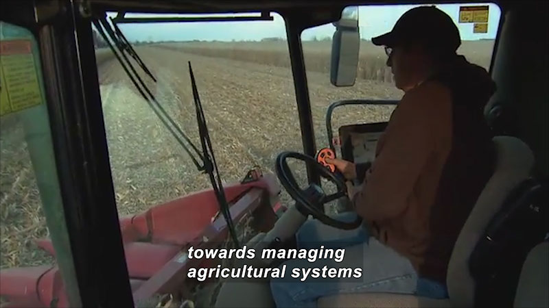 Person driving a large piece of industrial farm equipment. Caption: towards managing agricultural systems