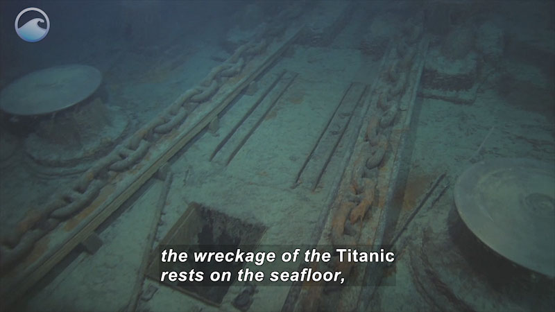 The deck of an underwater ship covered in debris and rusted metal. Caption: the wreckage of the Titanic rests on the seafloor,