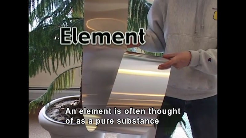 Person holding a sheet of a shiny metal. Caption: An element is often thought of as a pure substance