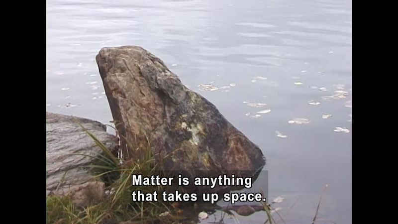 Chunk of rock sitting partially submerged in water. Caption: Matter is anything that takes up space.