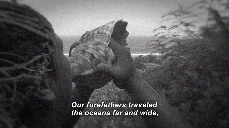 Person holding a shell to their mouth. Caption: Our forefathers traveled the oceans far and wide,